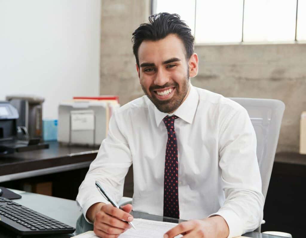 Un sonriente hombre de negocios que trabaja en una empresa de prop trading, garantizando la seguridad del capital mientras escribe diligentemente en un papel.