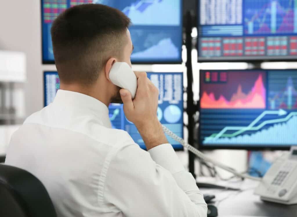 Un empresario de una empresa de prop trading'garantiza la seguridad del capital mientras conversa por teléfono entre varios monitores.